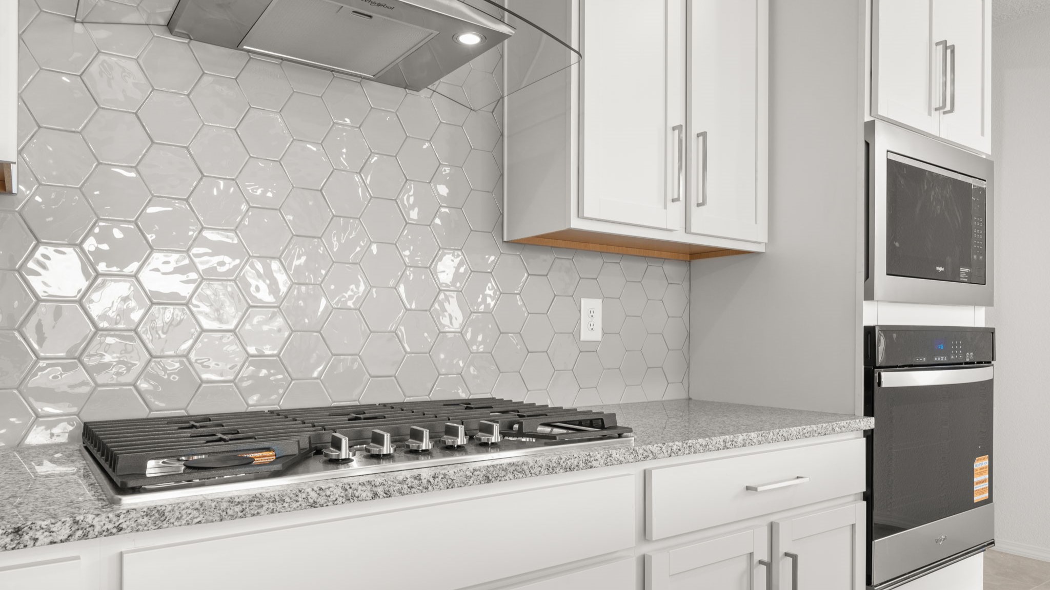 Kitchen with white cabinets, stainless steel appliances, and white and grey countertops.