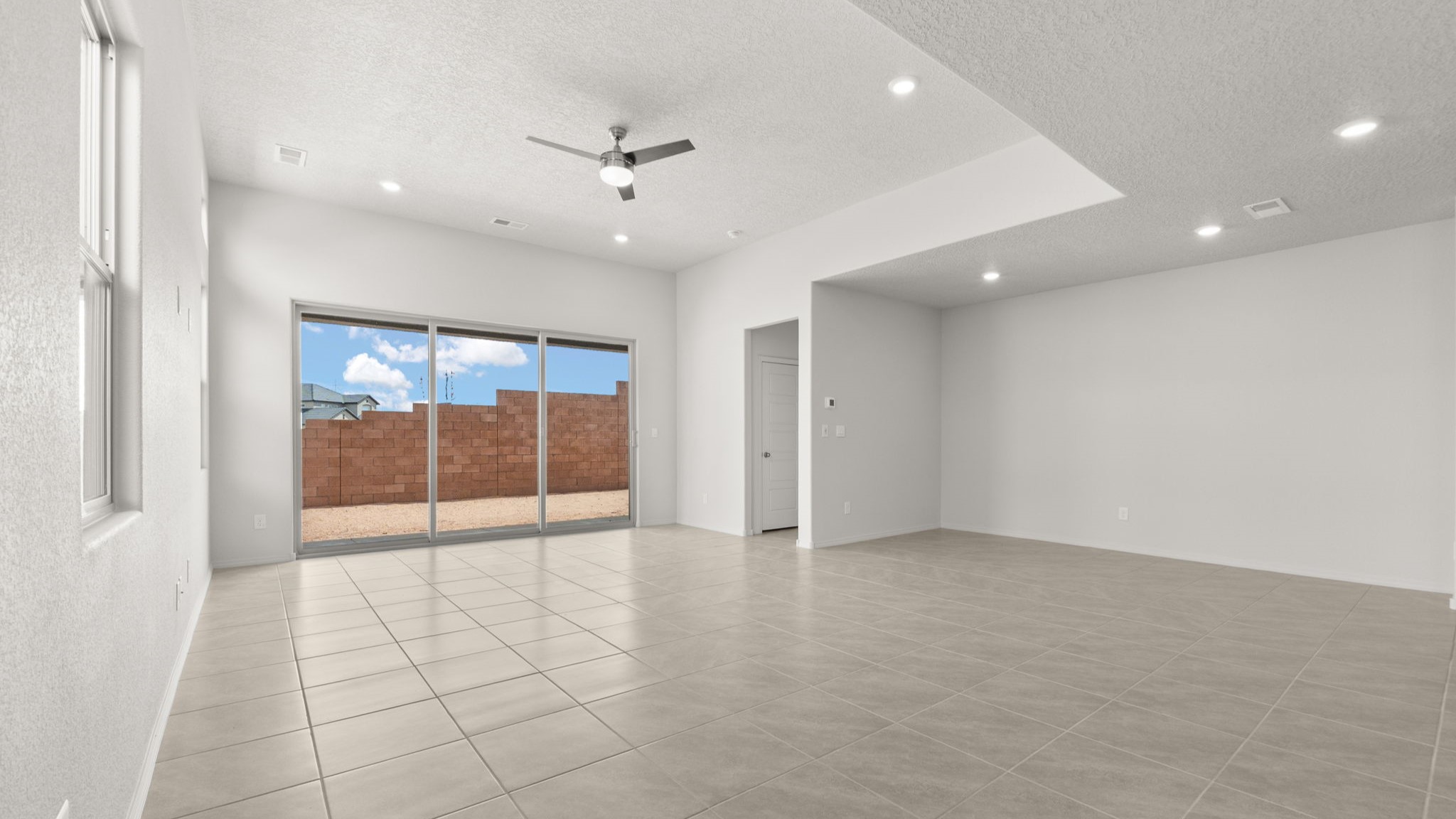 Living and dining area with white walls, light brown tile, and large windows.