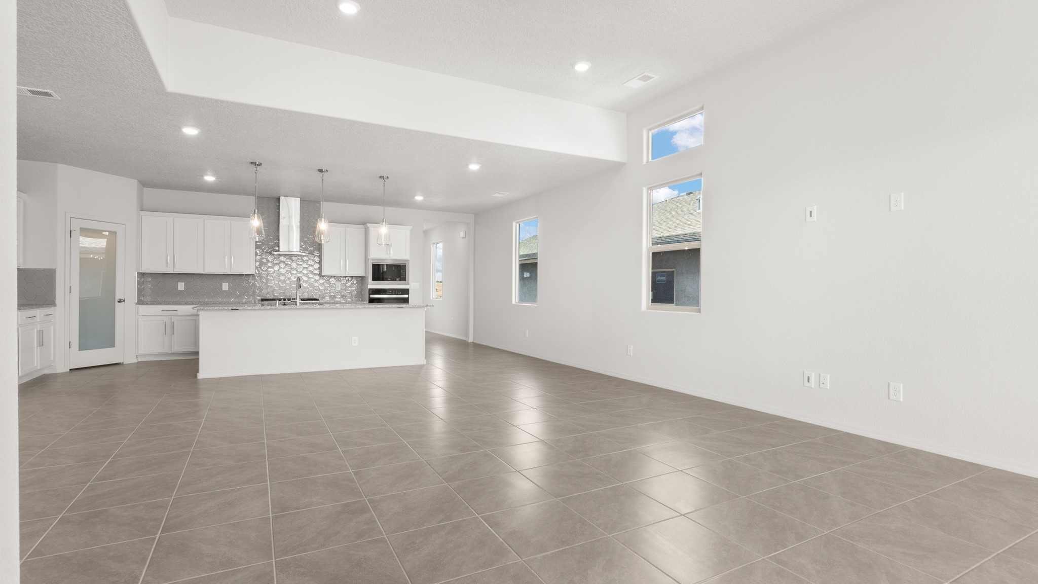 Living and dining area with white walls, light brown tile, and large windows.