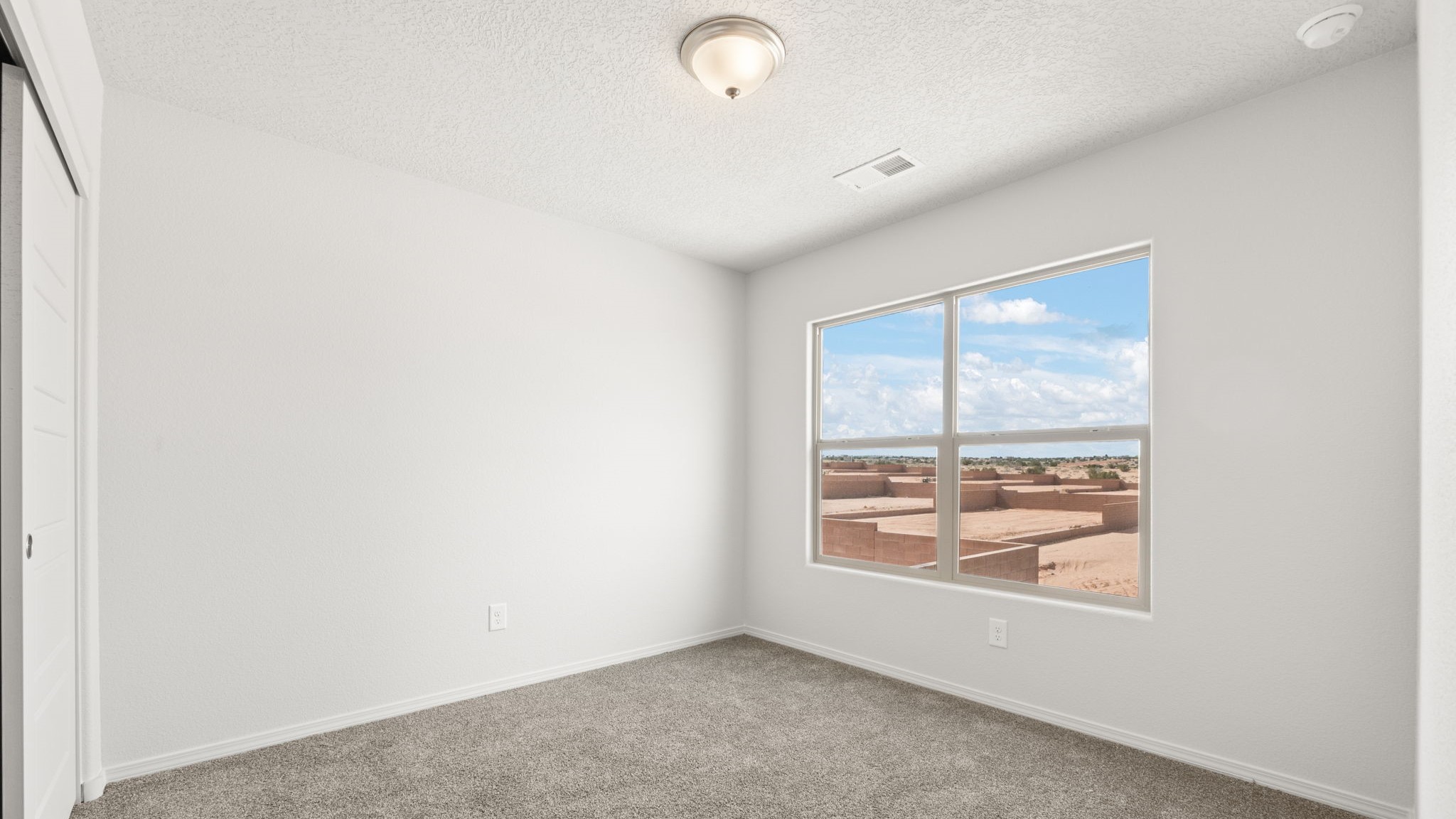 Bedroom with white walls, brown carpet, and a large window.