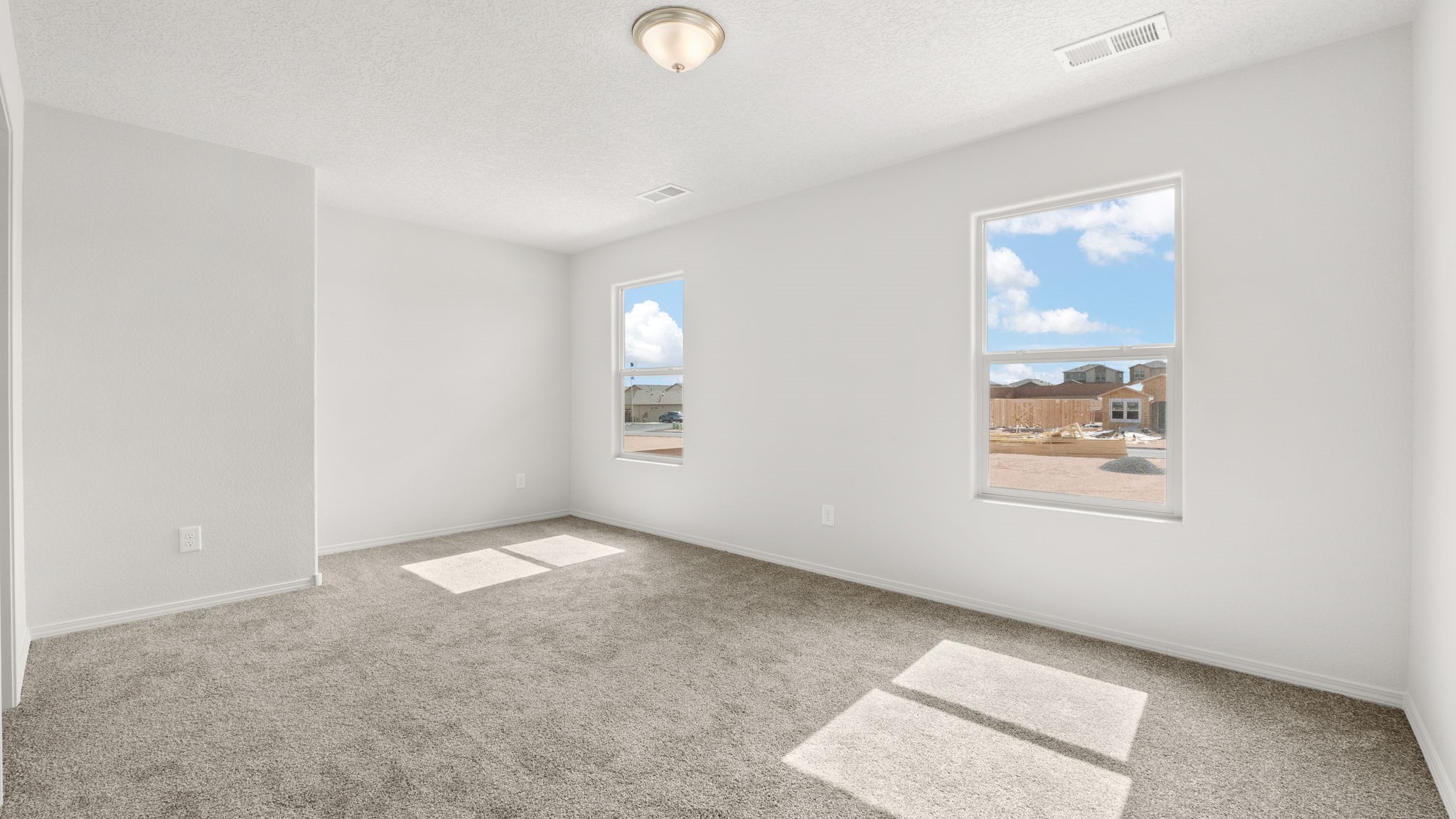 Bedroom with white walls, brown carpet, and large windows.