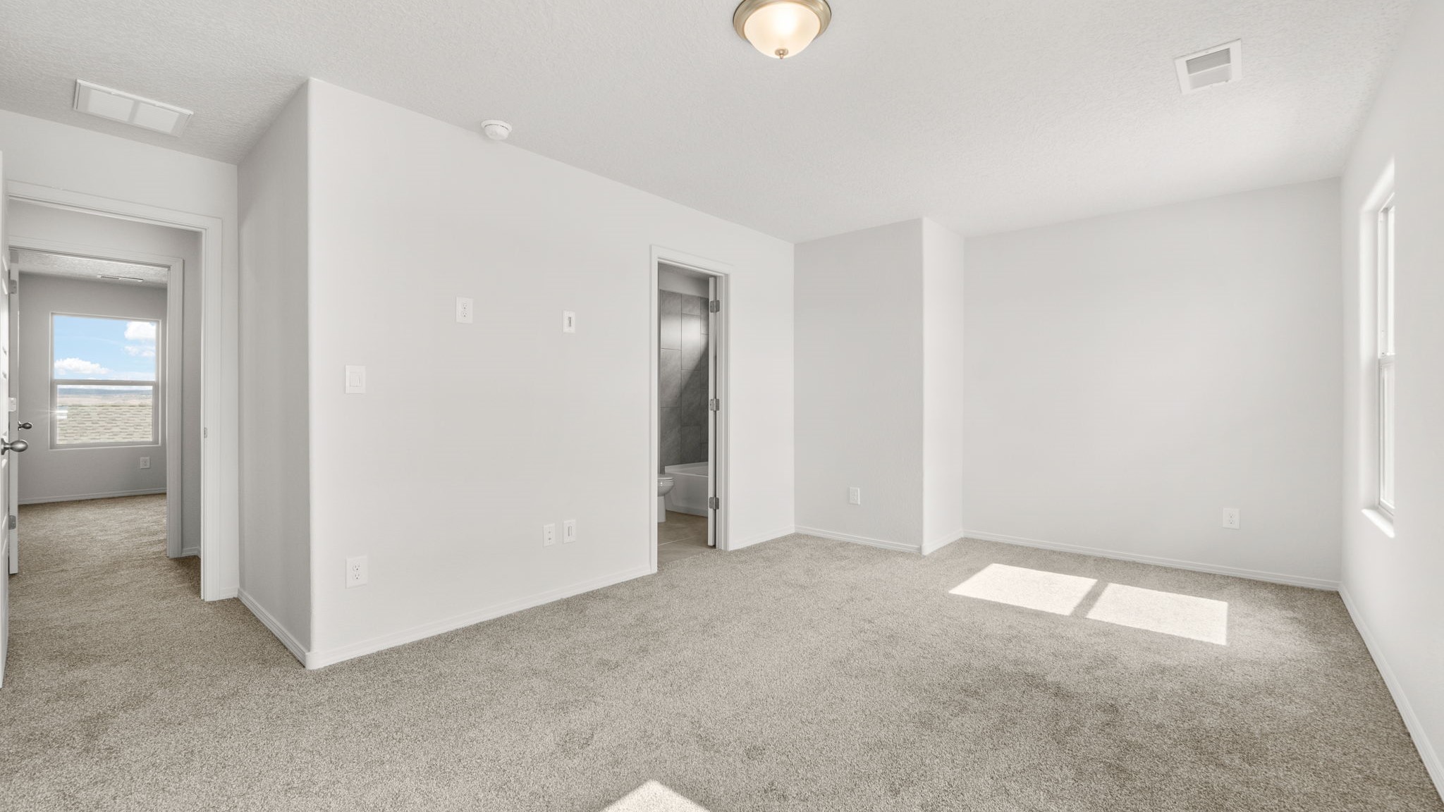 .Bedroom with white walls, brown carpet, and natural lighting.