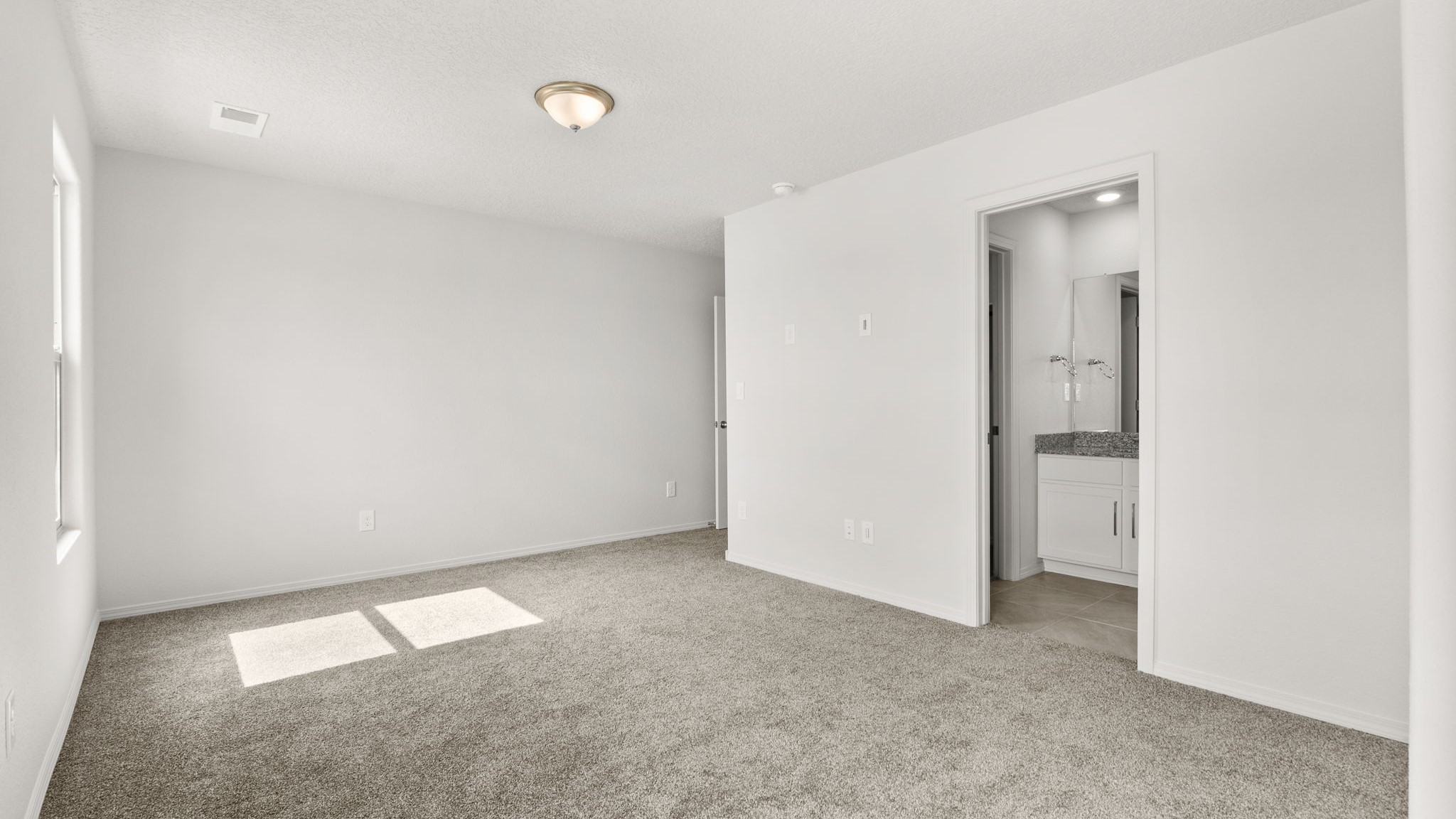 .Bedroom with white walls, brown carpet, and natural lighting.