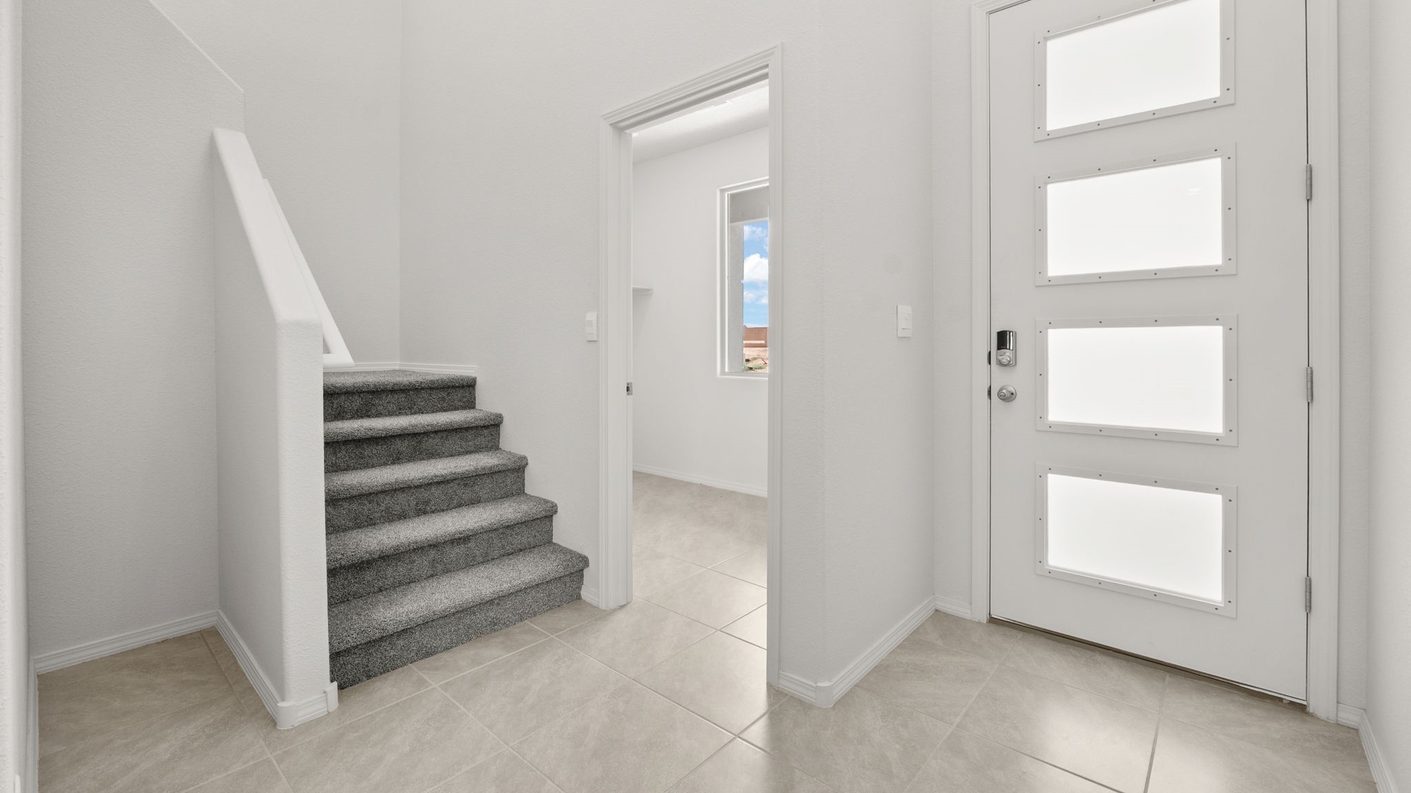 Entry way with white walls, light brown tile, and a staircase with grey carpet.