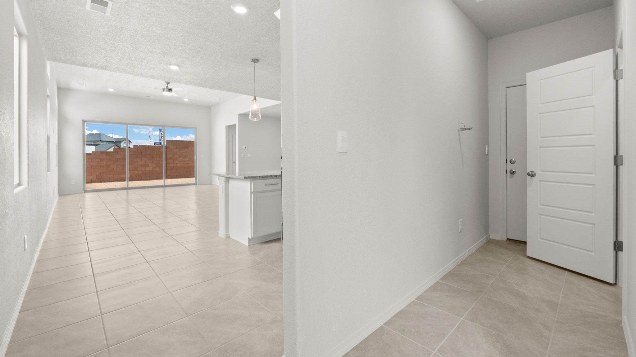 Entrance into the kitchen area with white walls, light brown tile, and large windows.
