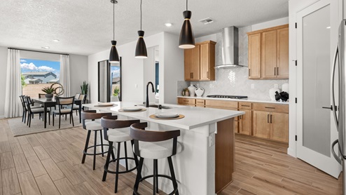 The Destin Kitchen with brown tile floors, white backsplash, kitchen island with granite countertops, and three pendant lights over the island.