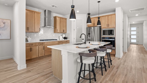 The Destin Kitchen with brown tile floors, white backsplash, kitchen island with granite countertops, and three pendant lights over the island.