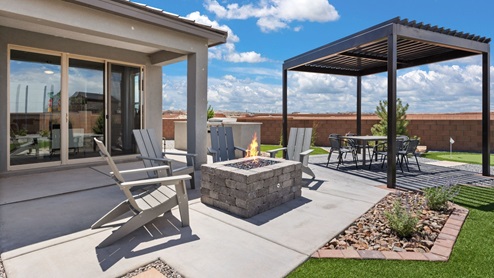 Model home backyard with outdoor kitchen, pergola, fire pit, and turf