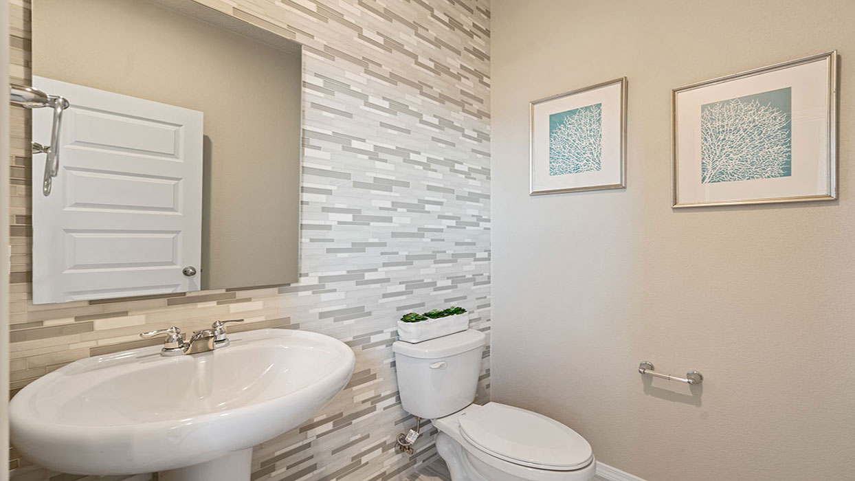 Half bath with pedestal sink, mirror, and upgraded fixtures near the front entry at Los Diamantes Phase III