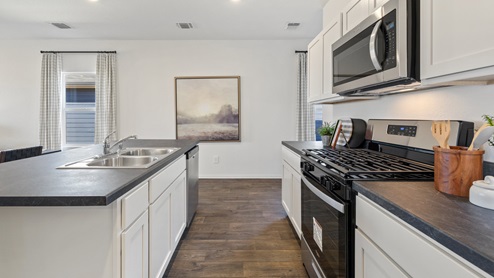 Side view of the kitchen area with granite countertops, large island, cabinets, tile backsplash, and stainless steel appliances with pantry in the corner.