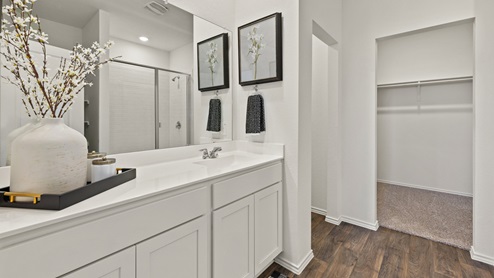 A modern bathroom featuring a double sink vanity with granite countertops and with spacious walk in closet and shower with built in shelves.