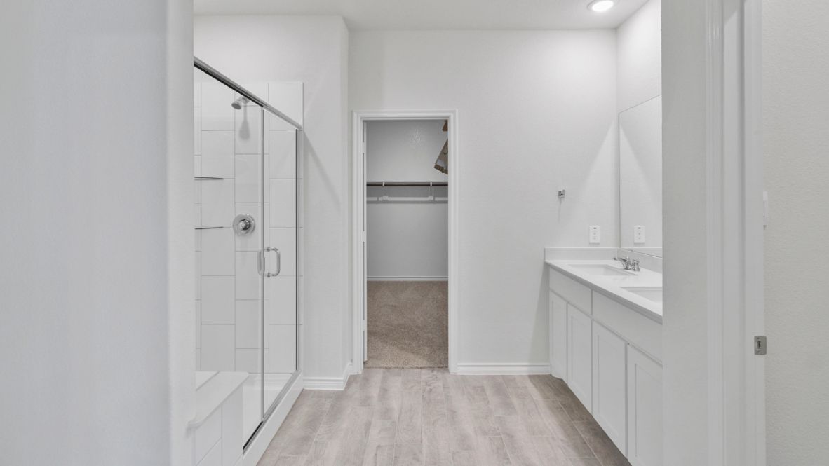 Spacious modern bathroom featuring a glass-enclosed shower, a large soaking tub with tiled surround and dual-sink vanity with sleek countertop. The layout includes a private water closet and a walk-in closet for added convenience, with natural light streaming through the window.