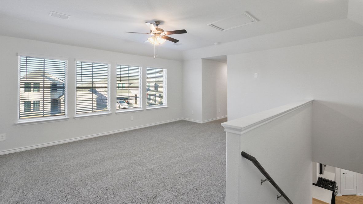 Open upstairs loft area with carpet flooring, multiple windows, and a ceiling fan for comfort.