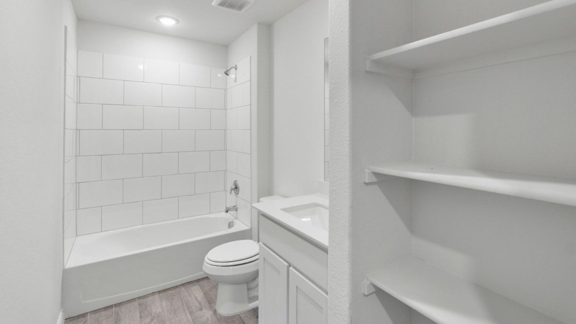 Modern secondary bathroom showcasing white cabinets, a sink, quartz countertops, and a 12x24 tiled shower surround.