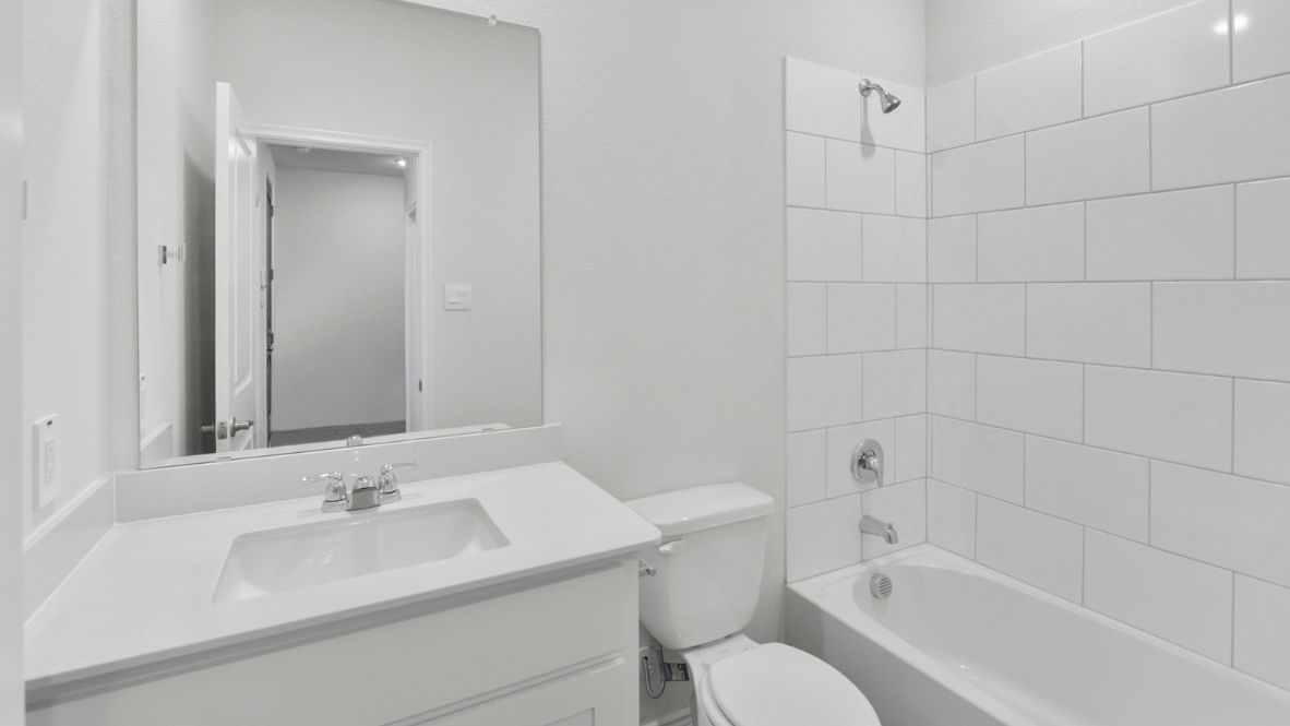 Modern secondary bathroom showcasing white cabinets, a sink, quartz countertops, and a 12x24 tiled shower surround.