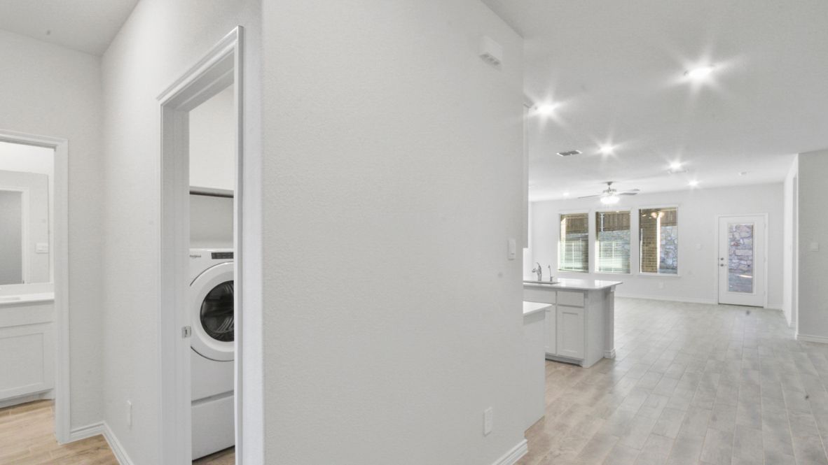 Open-concept kitchen and living area featuring a modern island with a stainless-steel sink and dishwasher, white cabinetry, and built-in appliances. The living room boasts a cozy fireplace, large windows allowing natural light, and wood-look flooring, creating a warm and inviting atmosphere.