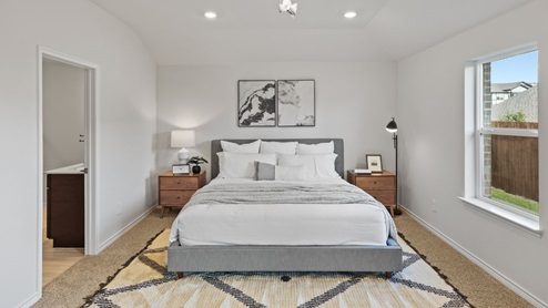 Spacious primary bedroom with beige carpet, white walls and two windows
