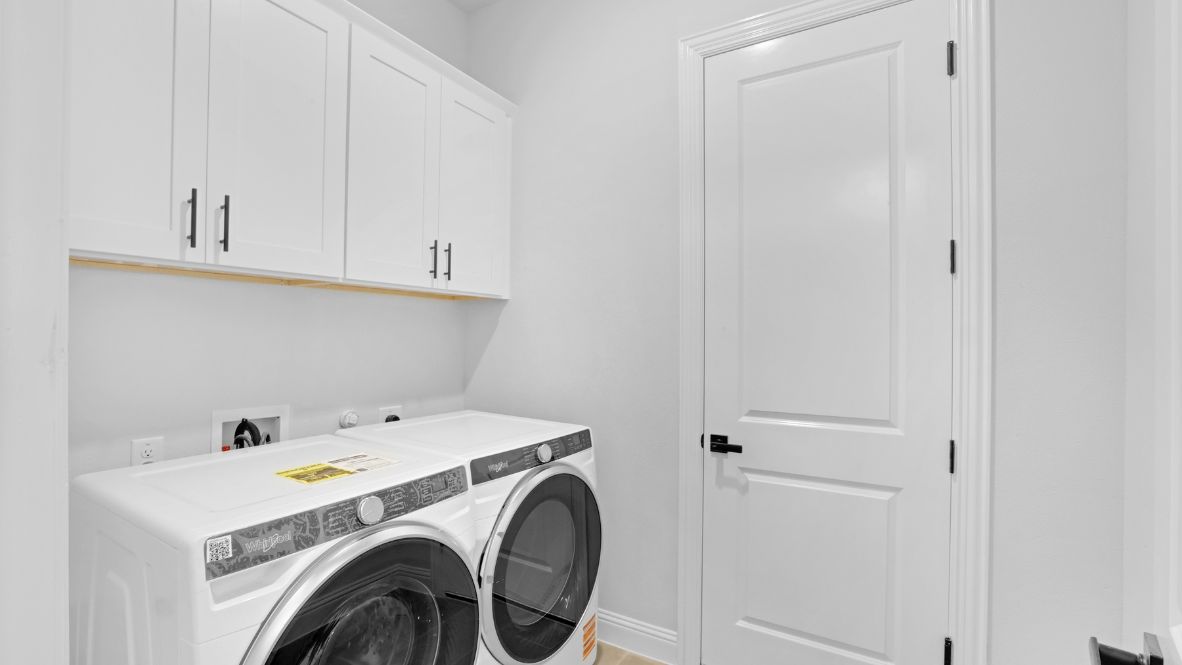 Laundry room with white cabinets above appliances.