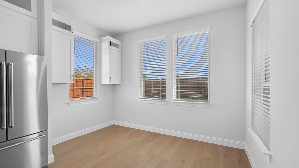 Dining area off the kitchen with light brown flooring and large windows.
