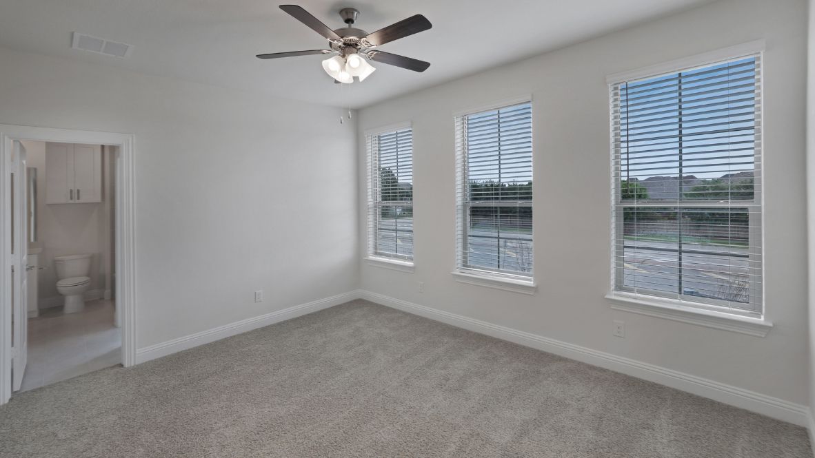 Spacious primary bedroom with beige carpet, white walls and windows