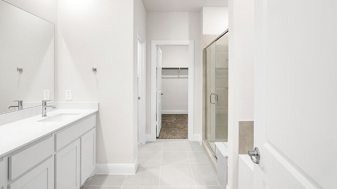 Spacious modern bathroom featuring a glass-enclosed shower, a large soaking tub with tiled surround and dual-sink vanity with sleek countertop. The layout includes a private water closet and a walk-in closet for added convenience, with natural light streaming through the window.