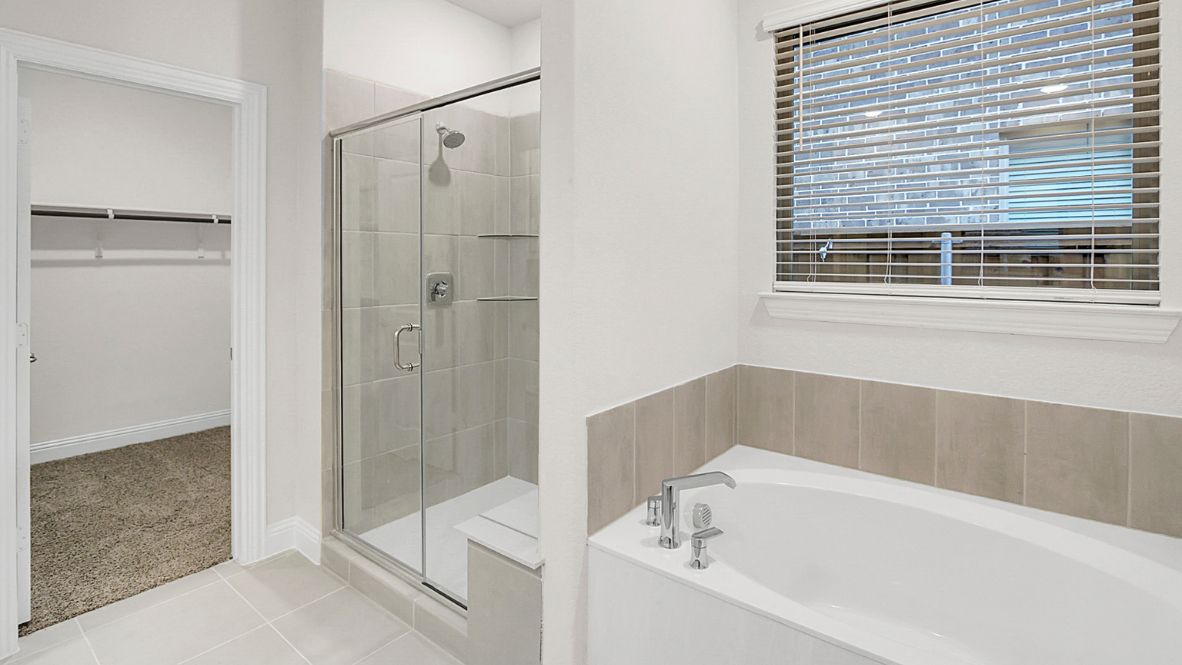 Spacious modern bathroom featuring a glass-enclosed shower, a large soaking tub with tiled surround and dual-sink vanity with sleek countertop. The layout includes a private water closet and a walk-in closet for added convenience, with natural light streaming through the window.