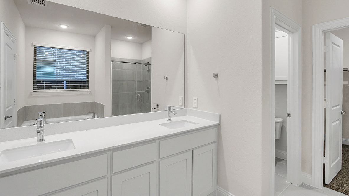Spacious modern bathroom featuring a glass-enclosed shower, a large soaking tub with tiled surround and dual-sink vanity with sleek countertop. The layout includes a private water closet and a walk-in closet for added convenience, with natural light streaming through the window.