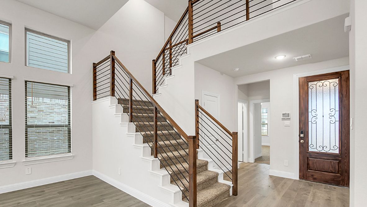 Bright and spacious open-concept kitchen and living area featuring modern white cabinetry, a large center island, and wood-look flooring. The design includes a loft with sleek railing, a high ceiling with ceiling fans, and carpeted stairs leading to the upper level.