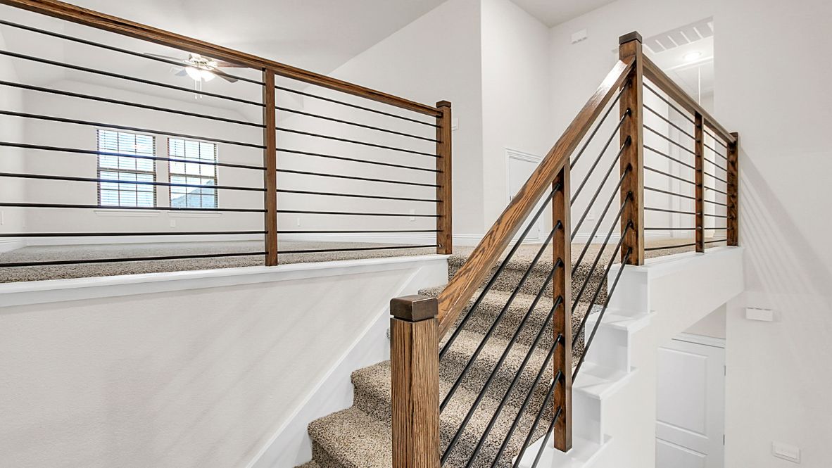 Bright and spacious open-concept kitchen and living area featuring modern white cabinetry, a large center island, and wood-look flooring. The design includes a loft with sleek railing, a high ceiling with ceiling fans, and carpeted stairs leading to the upper level.