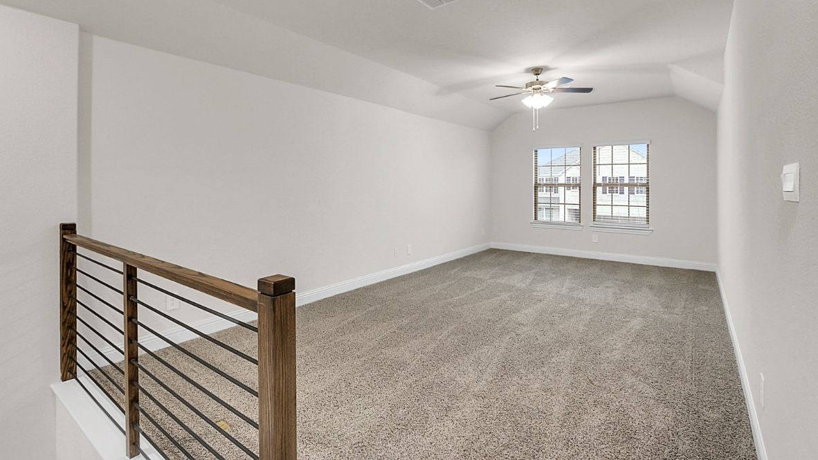 Bright and airy loft area with carpeted flooring, modern railing, and ceiling fan lighting. The open design overlooks the main living space below, creating a perfect spot for relaxation or additional living space.
