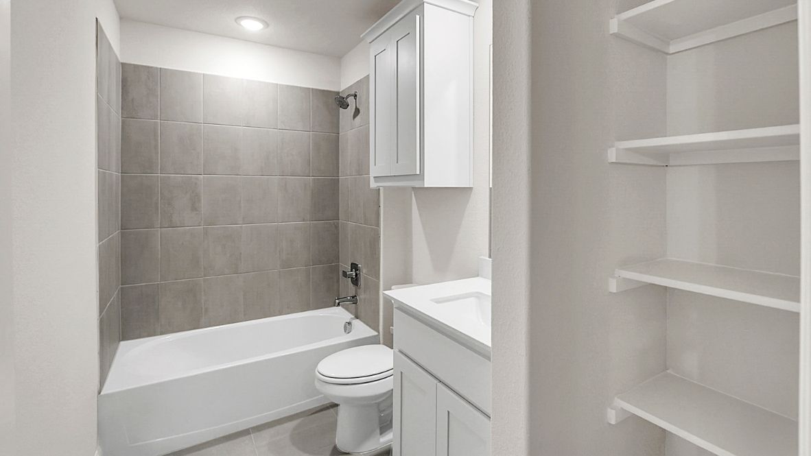 Modern secondary bathroom showcasing white cabinets, a sink, quartz countertops, and a 12x24 tiled shower surround.