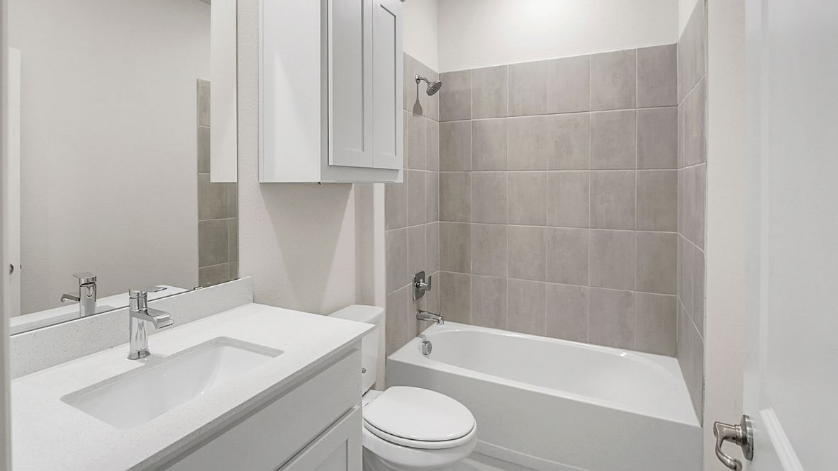 Modern secondary bathroom showcasing white cabinets, a sink, quartz countertops, and a 12x24 tiled shower surround.