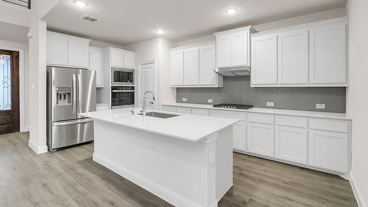 Bright and spacious open-concept kitchen and living area featuring modern white cabinetry, a large center island, and wood-look flooring. The design includes a loft with sleek railing, a high ceiling with ceiling fans, and carpeted stairs leading to the upper level.