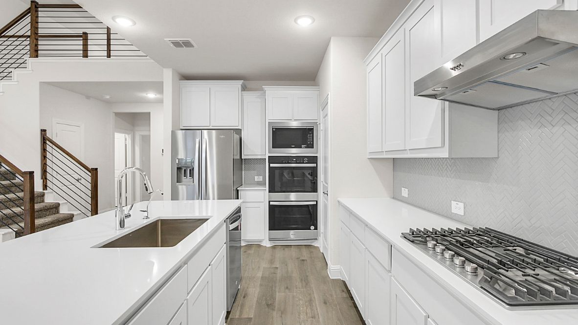 Bright and spacious open-concept kitchen and living area featuring modern white cabinetry, a large center island, and wood-look flooring. The design includes a loft with sleek railing, a high ceiling with ceiling fans, and carpeted stairs leading to the upper level.