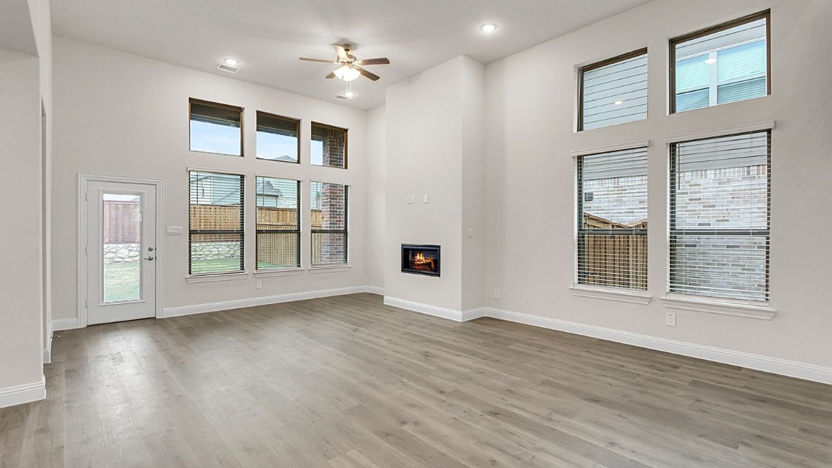 Open-concept kitchen and living area featuring a modern island with a stainless-steel sink and dishwasher, white cabinetry, and built-in appliances. The living room boasts a cozy fireplace, large windows allowing natural light, and wood-look flooring, creating a warm and inviting atmosphere.