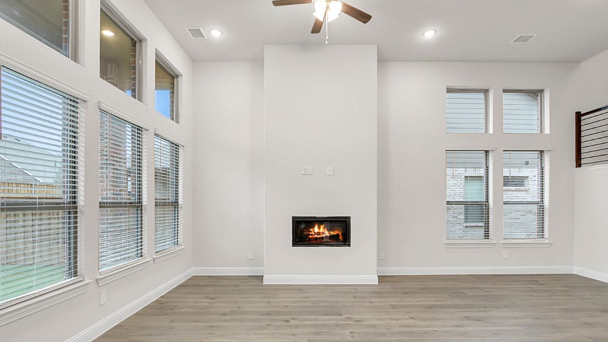 Open-concept kitchen and living area featuring a modern island with a stainless-steel sink and dishwasher, white cabinetry, and built-in appliances. The living room boasts a cozy fireplace, large windows allowing natural light, and wood-look flooring, creating a warm and inviting atmosphere.