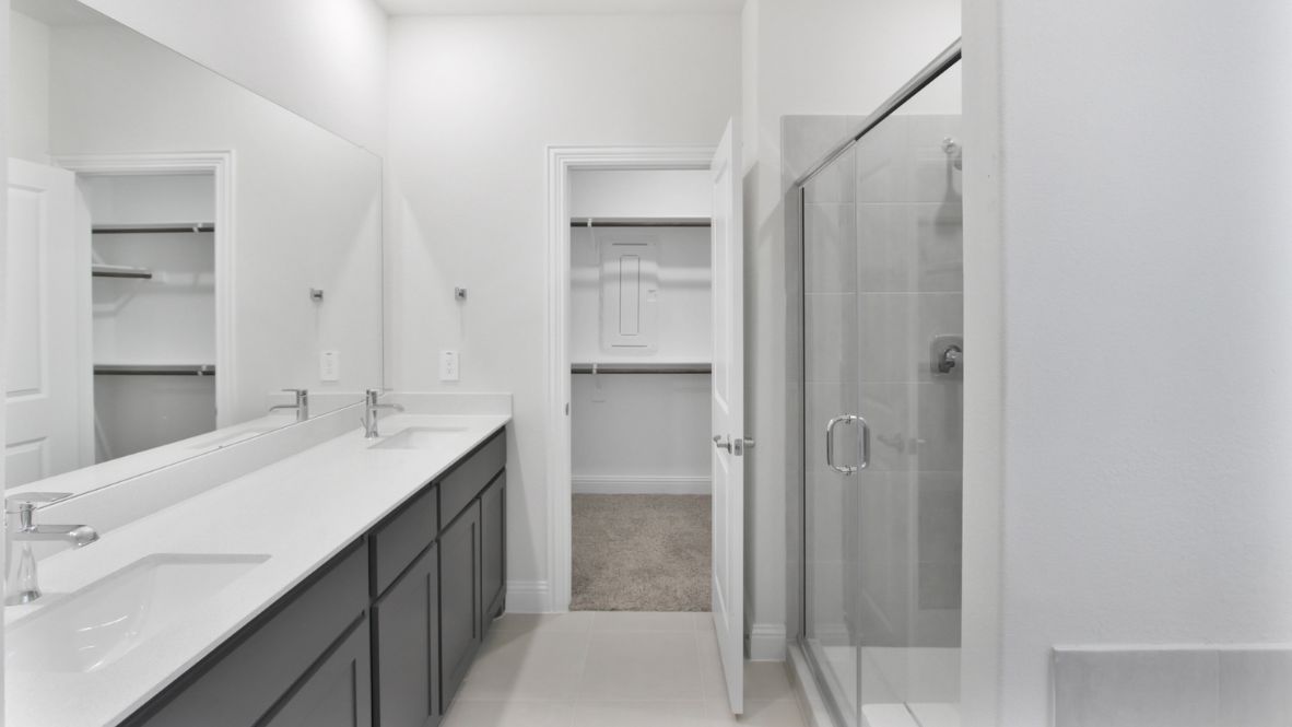 Spacious modern bathroom featuring a glass-enclosed shower, a large soaking tub with tiled surround and dual-sink vanity with sleek countertop. The layout includes a private water closet and a walk-in closet for added convenience, with natural light streaming through the window.