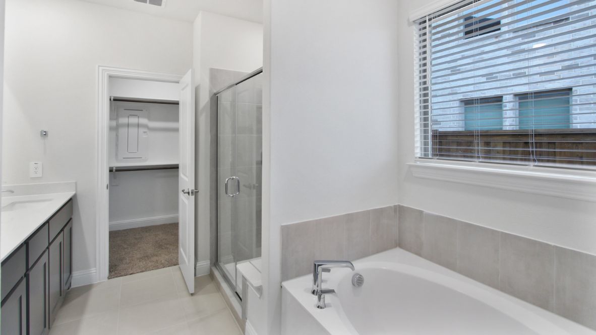 Spacious modern bathroom featuring a glass-enclosed shower, a large soaking tub with tiled surround and dual-sink vanity with sleek countertop. The layout includes a private water closet and a walk-in closet for added convenience, with natural light streaming through the window.