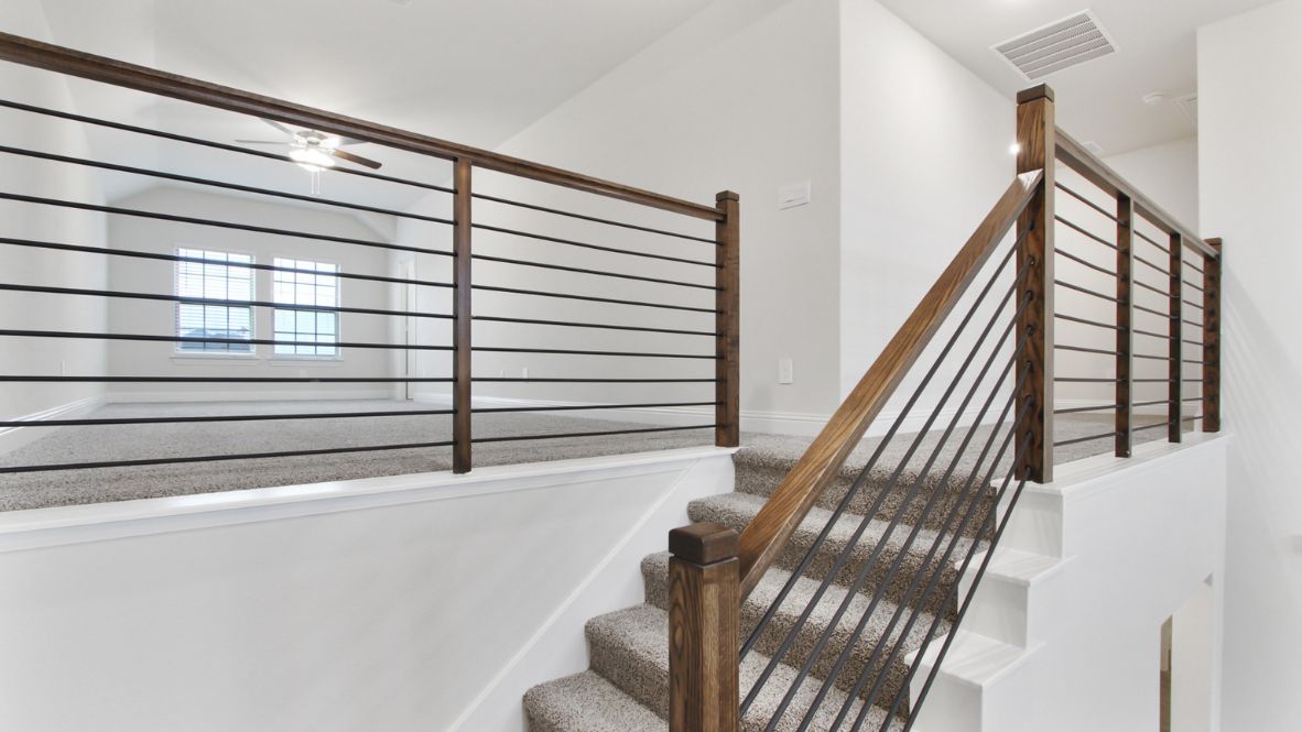 Bright and airy loft area with carpeted flooring, modern railing, and ceiling fan lighting. The open design overlooks the main living space below, creating a perfect spot for relaxation or additional living space.