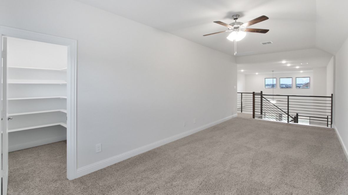 Bright and airy loft area with carpeted flooring, modern railing, and ceiling fan lighting. The open design overlooks the main living space below, creating a perfect spot for relaxation or additional living space.