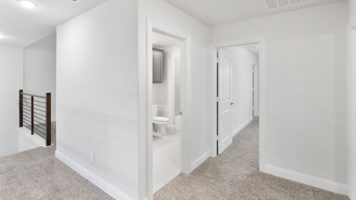 Bright and airy loft area with carpeted flooring, modern railing, and ceiling fan lighting. The open design overlooks the main living space below, creating a perfect spot for relaxation or additional living space.