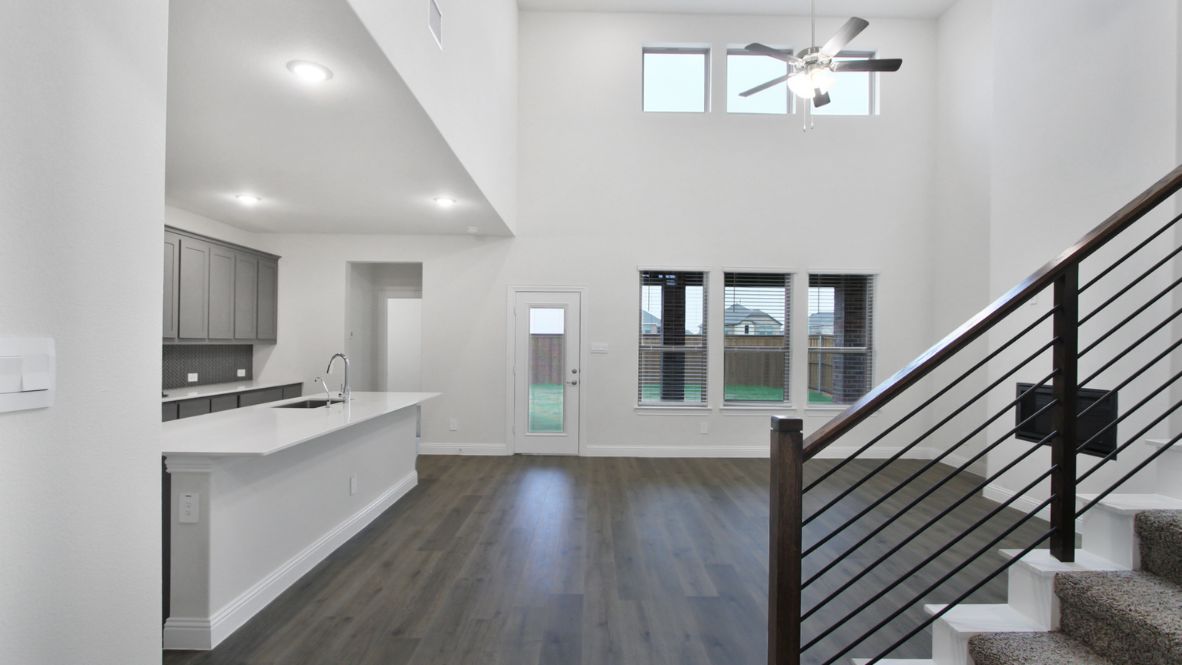 Open-concept kitchen and living area featuring a modern island with a stainless-steel sink and dishwasher, white cabinetry, and built-in appliances. The living room boasts a cozy fireplace, large windows allowing natural light, and wood-look flooring, creating a warm and inviting atmosphere.