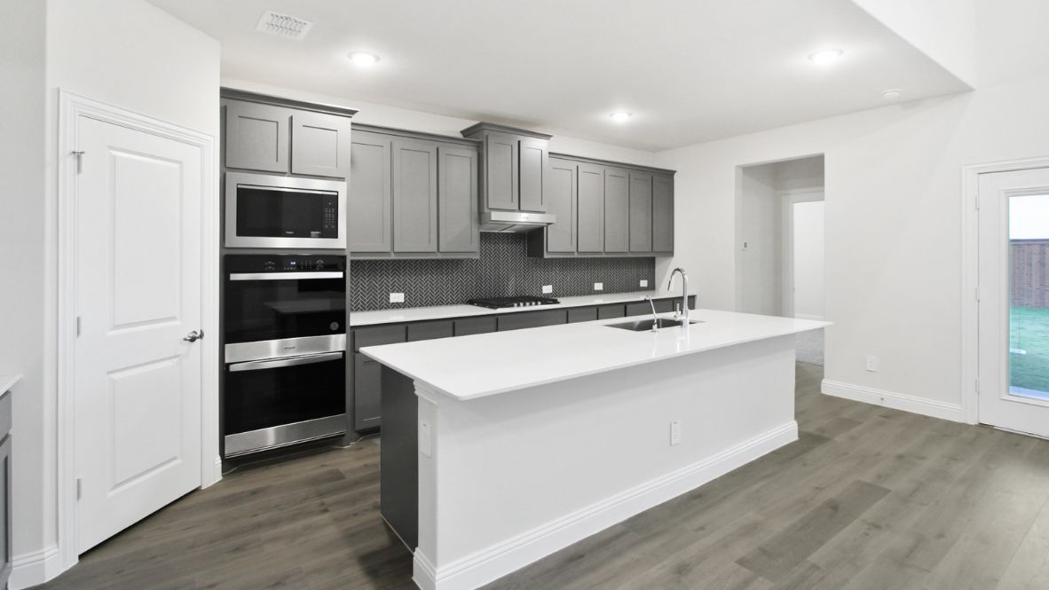 Bright and spacious open-concept kitchen and living area featuring modern white cabinetry, a large center island, and wood-look flooring. The design includes a loft with sleek railing, a high ceiling with ceiling fans, and carpeted stairs leading to the upper level.