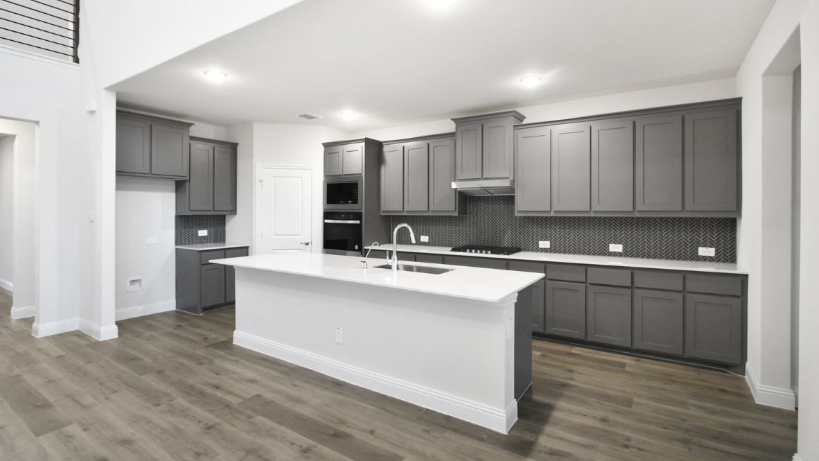 Bright and spacious open-concept kitchen and living area featuring modern white cabinetry, a large center island, and wood-look flooring. The design includes a loft with sleek railing, a high ceiling with ceiling fans, and carpeted stairs leading to the upper level.