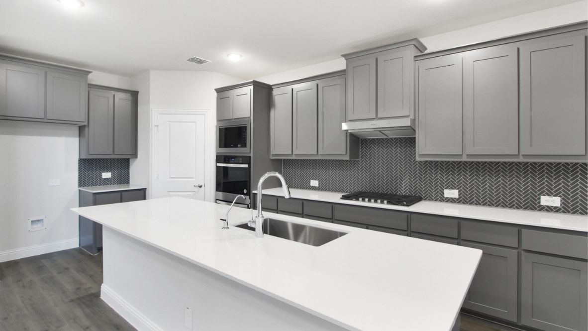 Bright and spacious open-concept kitchen and living area featuring modern white cabinetry, a large center island, and wood-look flooring. The design includes a loft with sleek railing, a high ceiling with ceiling fans, and carpeted stairs leading to the upper level.