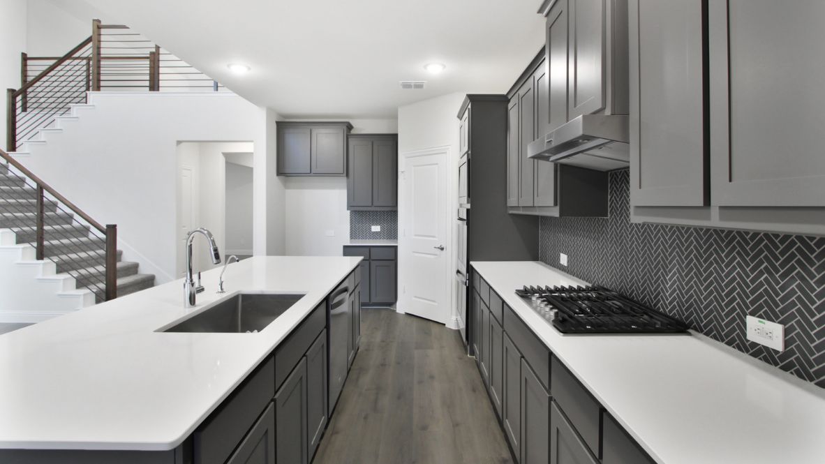 Bright and spacious open-concept kitchen and living area featuring modern white cabinetry, a large center island, and wood-look flooring. The design includes a loft with sleek railing, a high ceiling with ceiling fans, and carpeted stairs leading to the upper level.