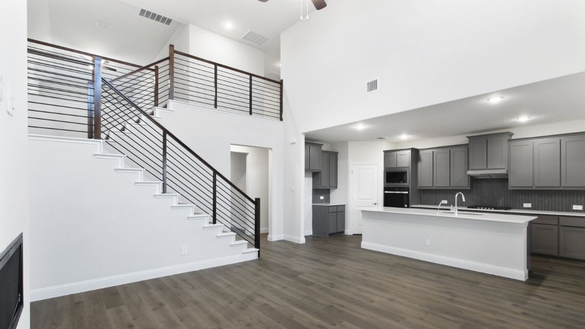 Modern open-concept living room with cozy fireplace, large windows offering natural light, and wood-look flooring. The space features a contemporary staircase with sleep railing leading to an upper loft area, and a view of the bright kitchen with white cabinetry, stainless steel appliances, and a spacious island.