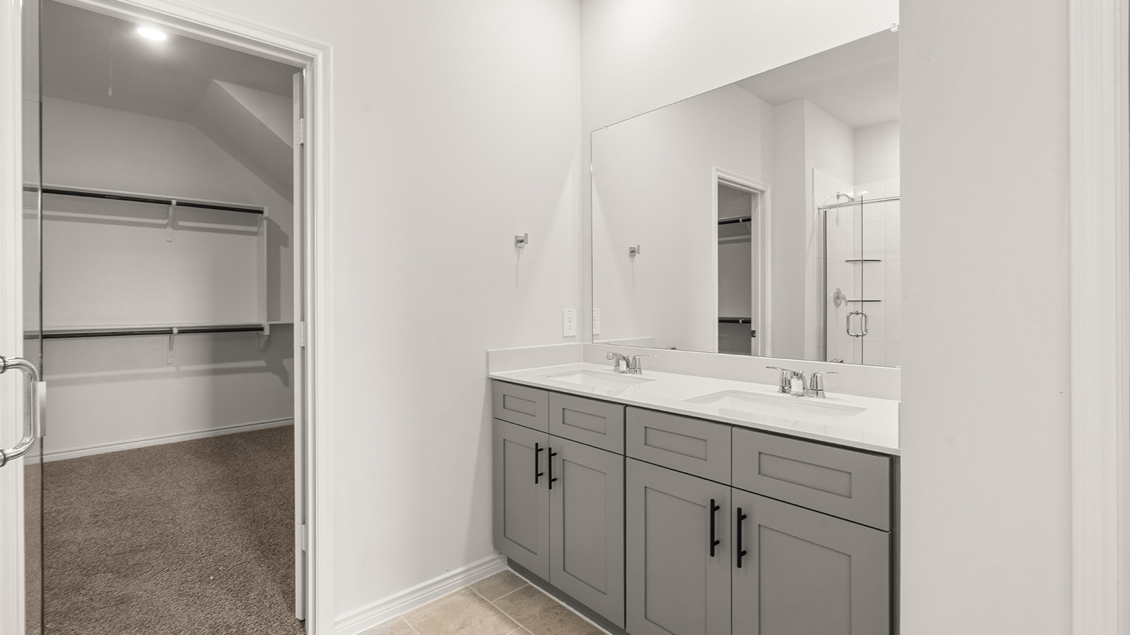 Modern primary bathroom with double vanities, granite countertops, and a glass-enclosed shower with a walk-in closet.