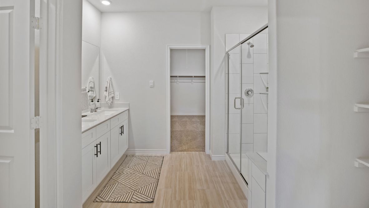 Modern primary bathroom with double vanities, granite countertops, and a glass-enclosed shower with a walk-in closet.