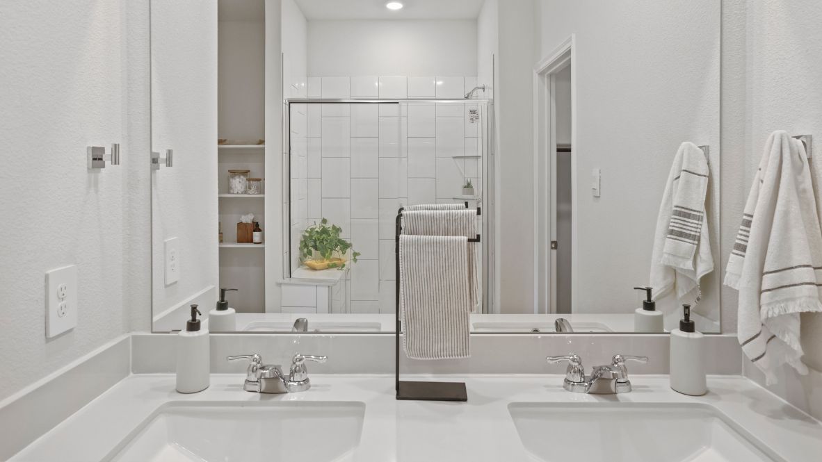 Modern primary bathroom with double vanities, granite countertops, and a glass-enclosed shower with a walk-in closet.